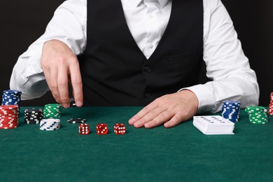 Photo of Professional croupier at gambling table with casino chips, playing cards and dice, closeup