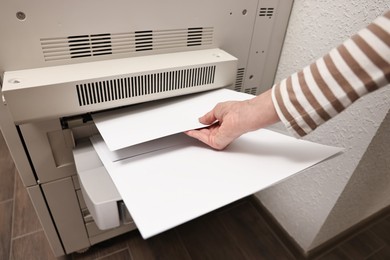 Photo of Woman using modern printer indoors, closeup. Printing house