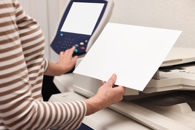 Photo of Woman with paper sheet using modern printer indoors, closeup. Printing house