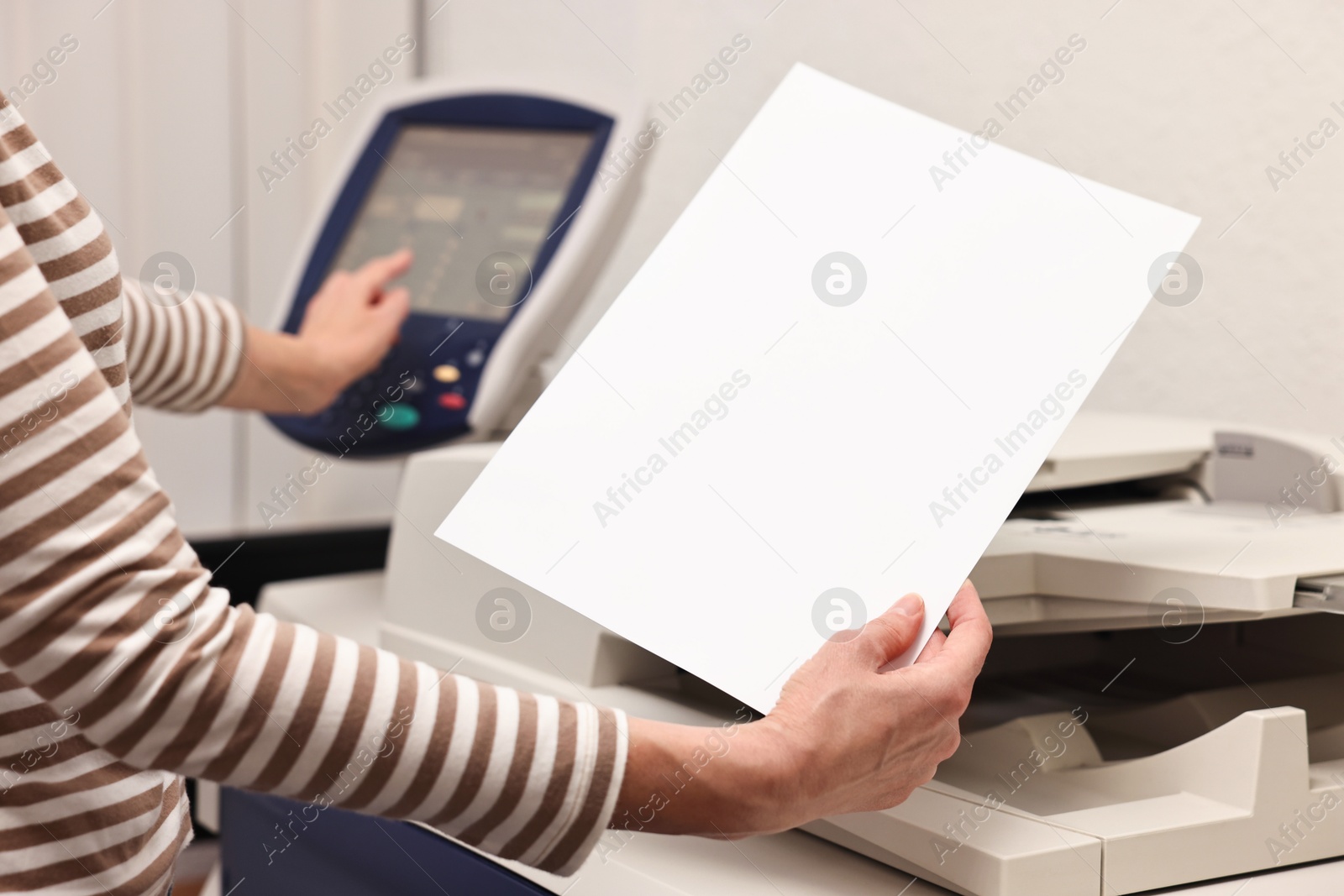 Photo of Woman with paper sheet using modern printer indoors, closeup. Printing house