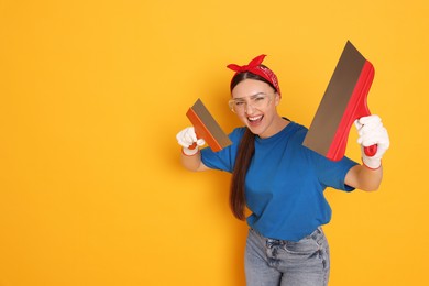 Photo of Portrait of young decorator with putty knives on orange background, space for text