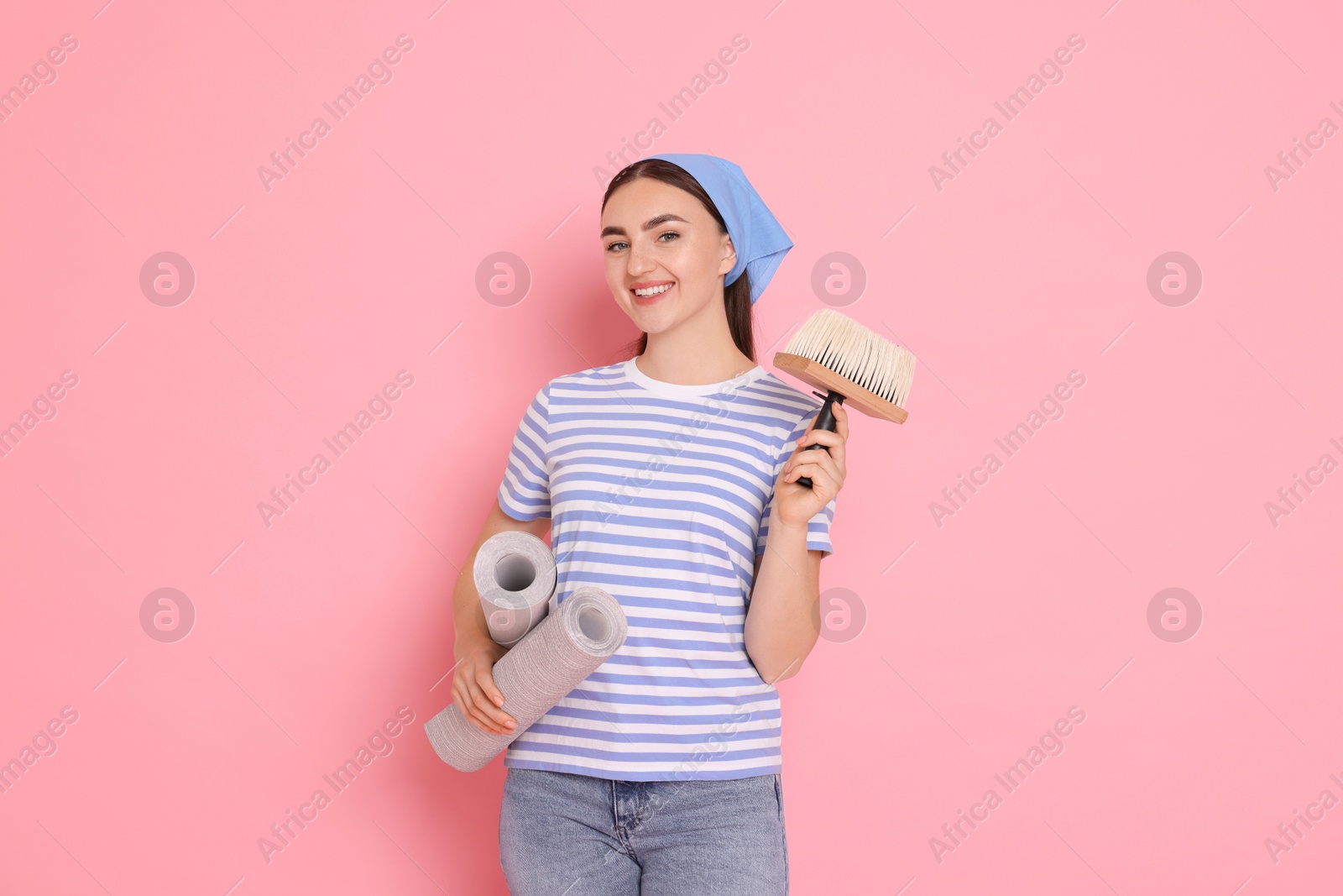 Photo of Young decorator with rolls of wallpaper and brush on pink background