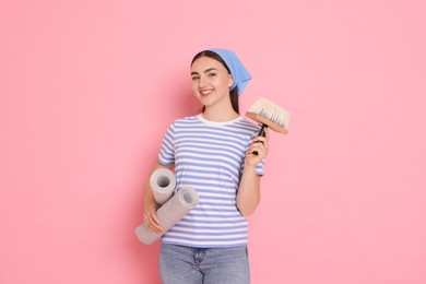 Young decorator with rolls of wallpaper and brush on pink background