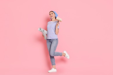 Young decorator with rolls of wallpaper and brush on pink background