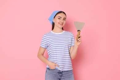 Portrait of young decorator with putty knife on pink background