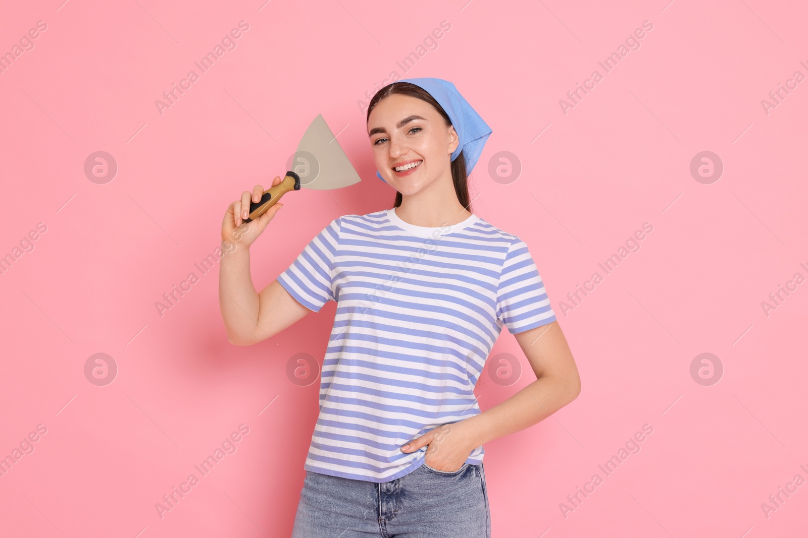 Photo of Portrait of young decorator with putty knife on pink background