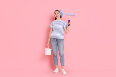 Photo of Young decorator with paint roller and bucket on pink background