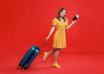 Photo of Happy traveller with suitcase, passport and ticket on red background