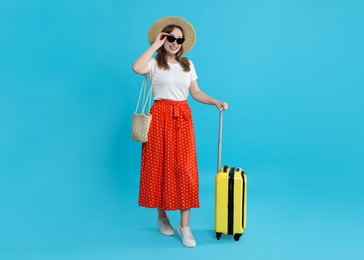 Photo of Happy traveller in sunglasses with suitcase on light blue background