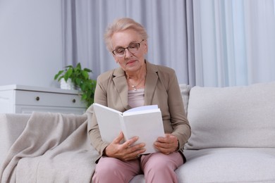 Photo of Senior woman reading book on sofa at home