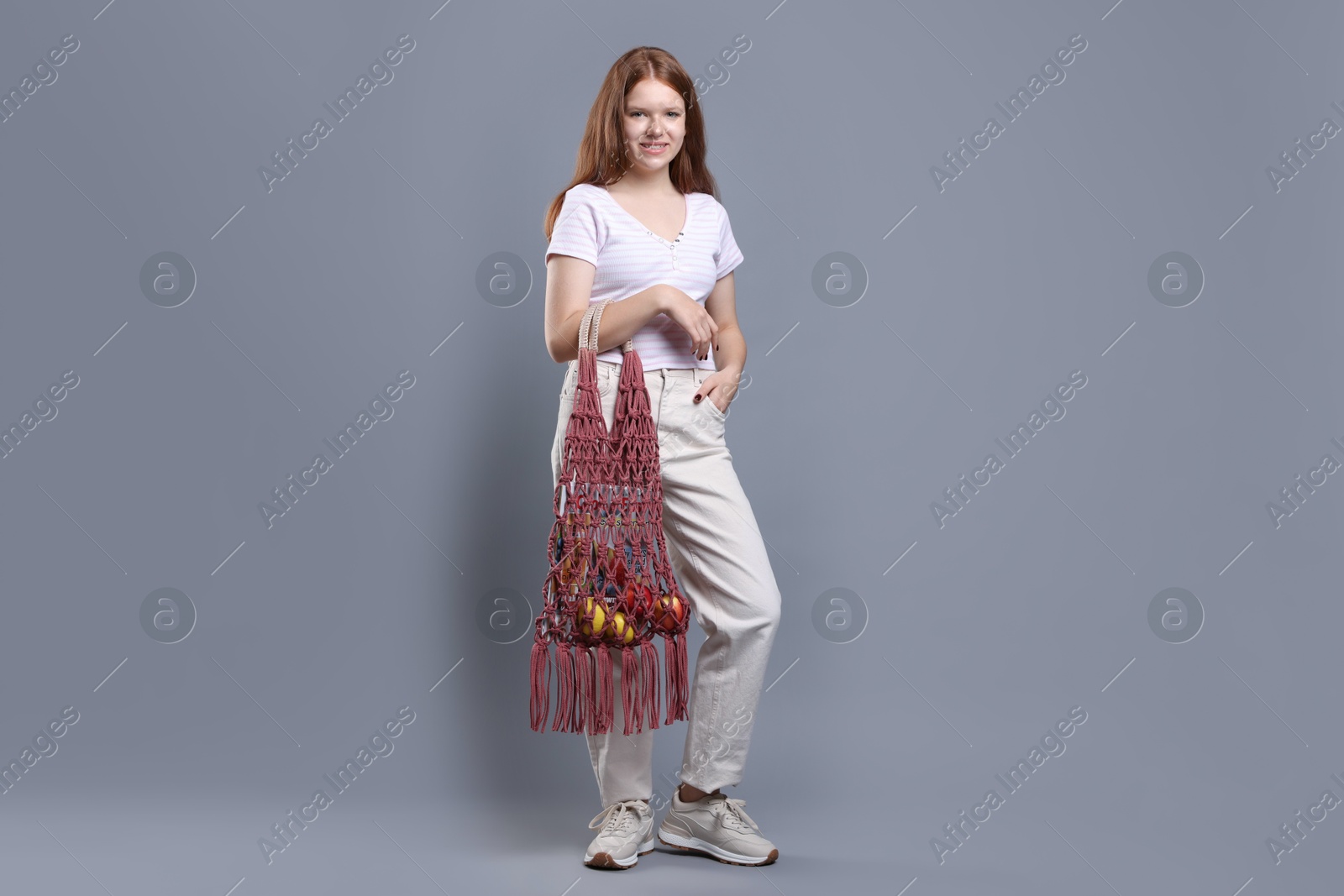 Photo of Teenage girl with handmade macrame bag on grey background