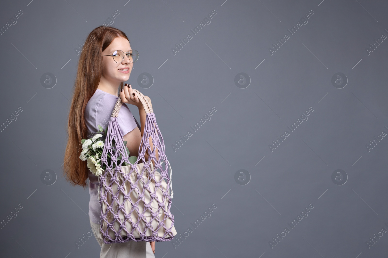 Photo of Teenage girl with handmade macrame bag on grey background. Space for text