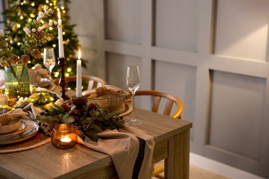 Photo of Christmas celebration. Festive table setting with dishware, glasses and decor in room