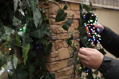 Photo of Man decorating house with Christmas lights outdoors, closeup