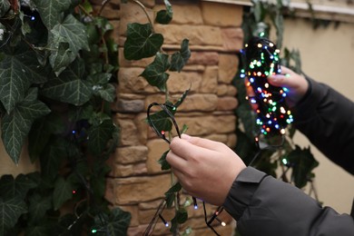 Photo of Man decorating house with Christmas lights outdoors, closeup