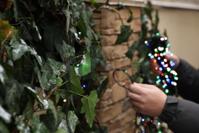 Photo of Man decorating house with Christmas lights outdoors, closeup