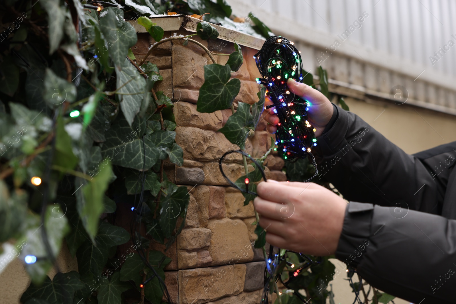 Photo of Man decorating house with Christmas lights outdoors, closeup