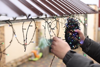 Photo of Man decorating house with Christmas lights outdoors, closeup