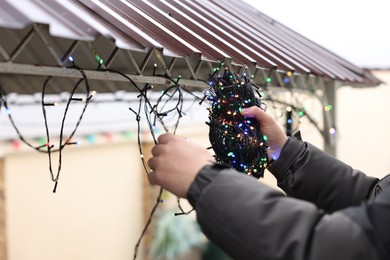 Photo of Man decorating house with Christmas lights outdoors, closeup