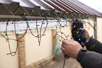 Photo of Man decorating house with Christmas lights outdoors, closeup