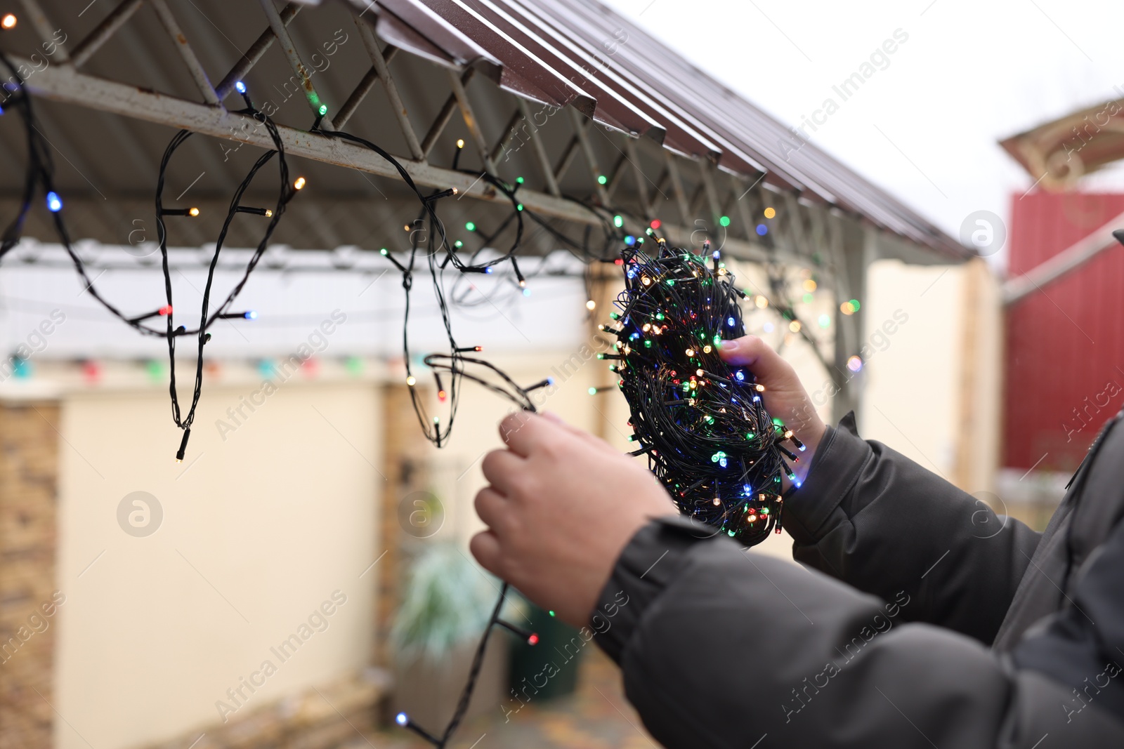 Photo of Man decorating house with Christmas lights outdoors, closeup