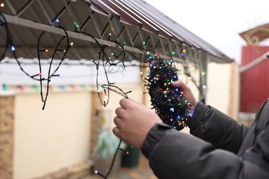 Photo of Man decorating house with Christmas lights outdoors, closeup