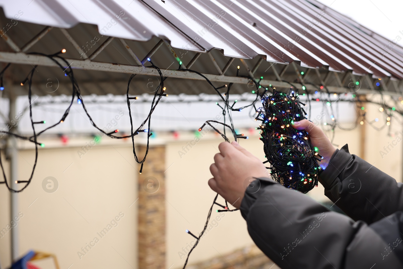 Photo of Man decorating house with Christmas lights outdoors, closeup