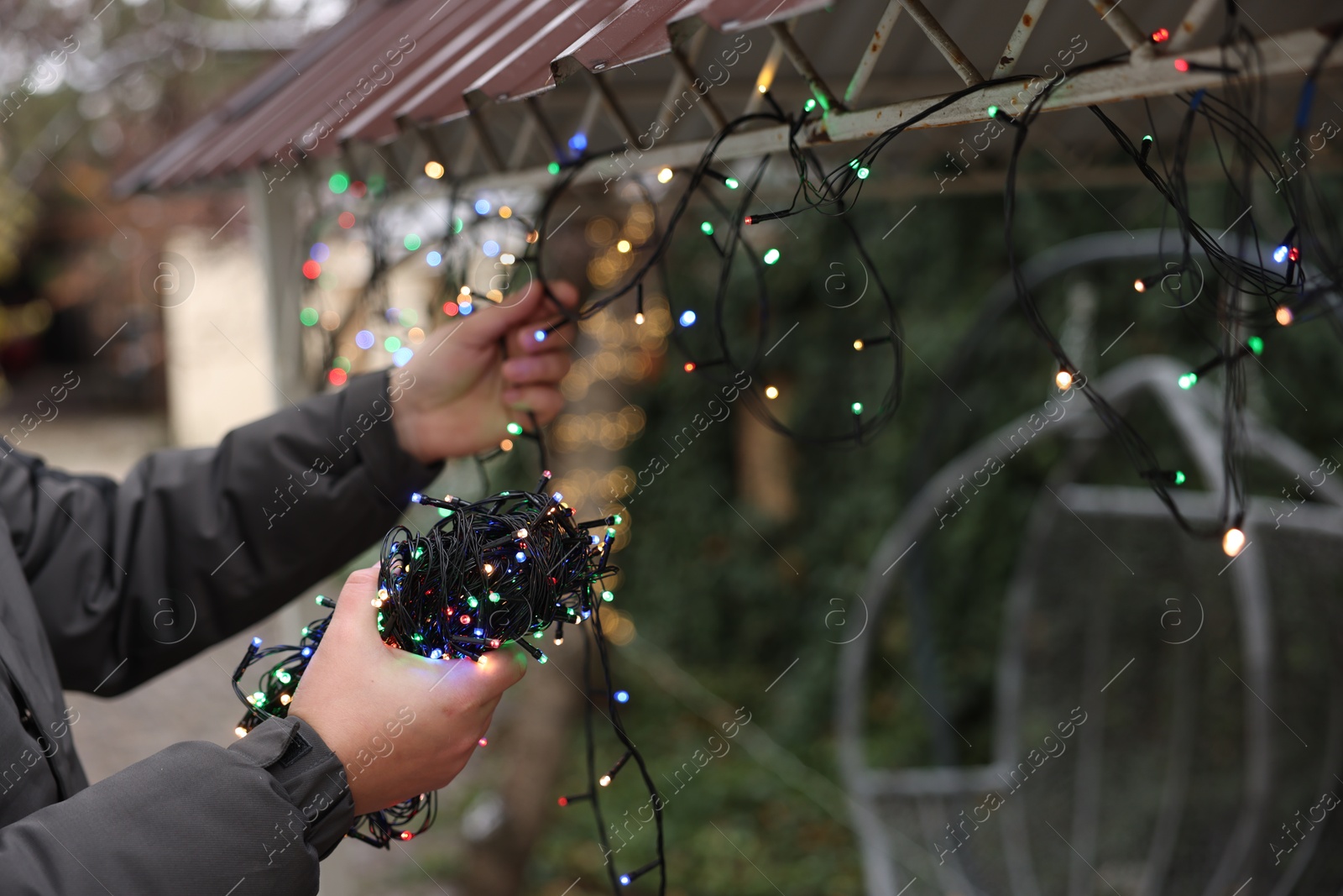 Photo of Man decorating house with Christmas lights outdoors, closeup