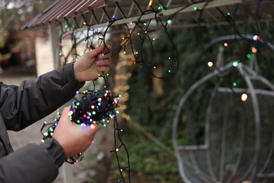 Photo of Man decorating house with Christmas lights outdoors, closeup