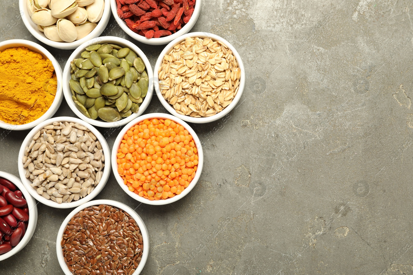 Photo of Different superfoods in bowls on grey table, flat lay. Space for text