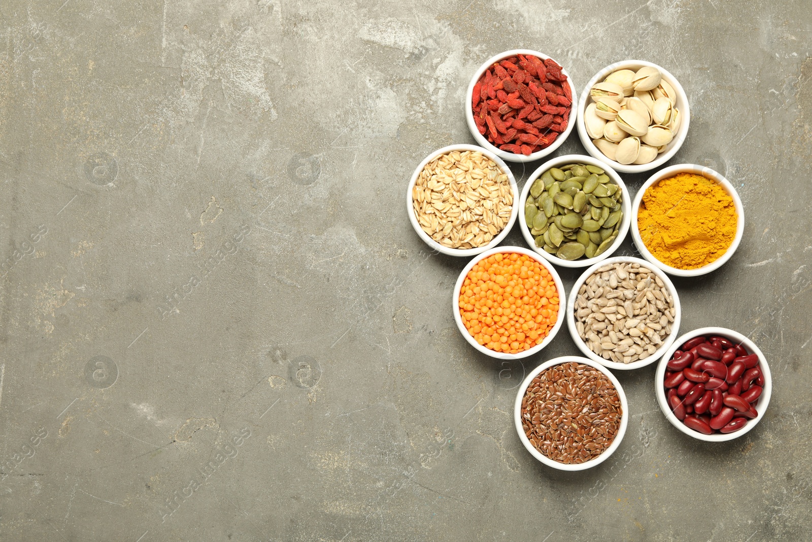 Photo of Different superfoods in bowls on grey table, flat lay. Space for text