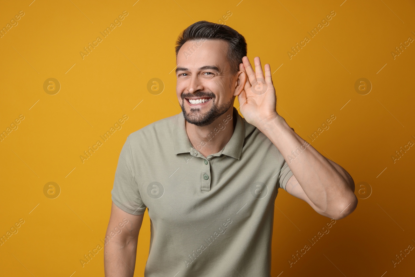 Photo of Man showing hand to ear gesture on orange background