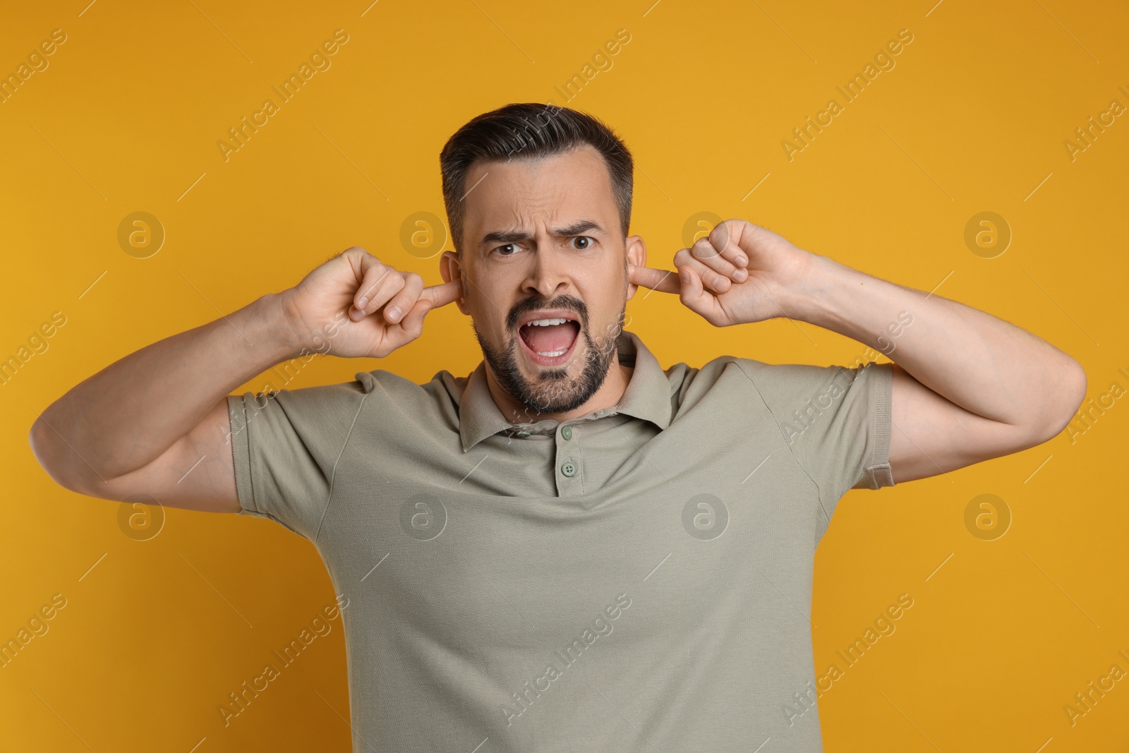 Photo of Man covering his ears with fingers on orange background