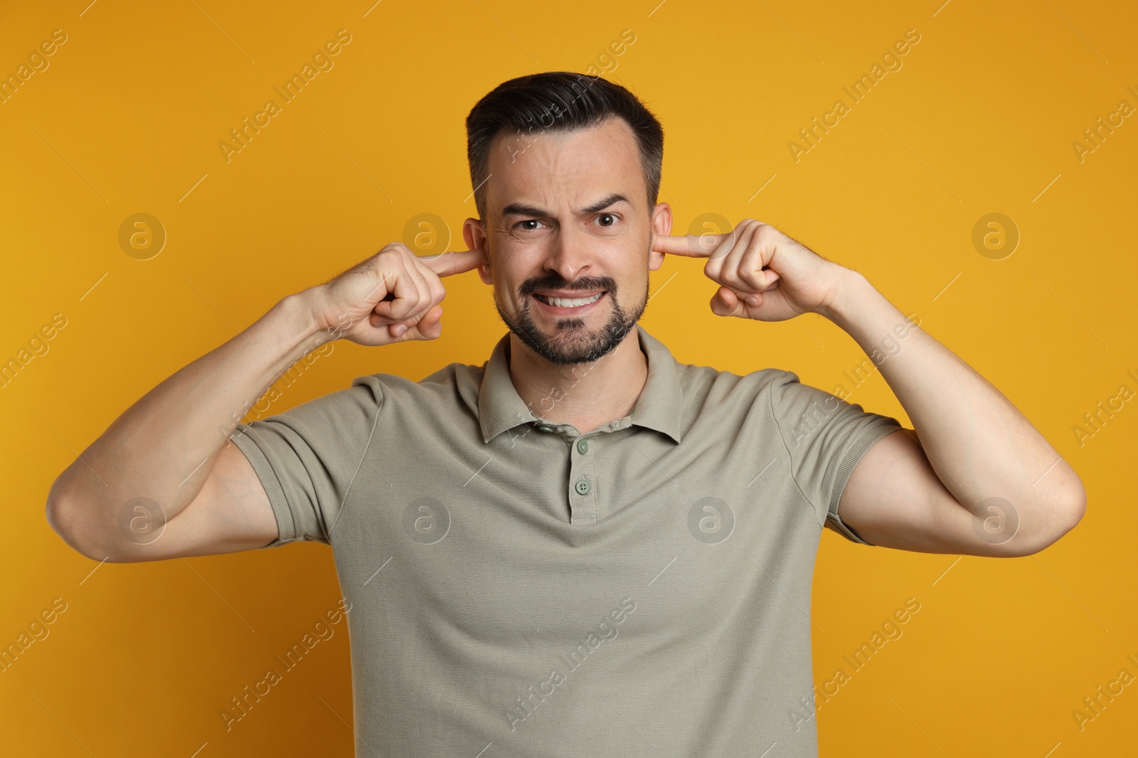 Photo of Man covering his ears with fingers on orange background