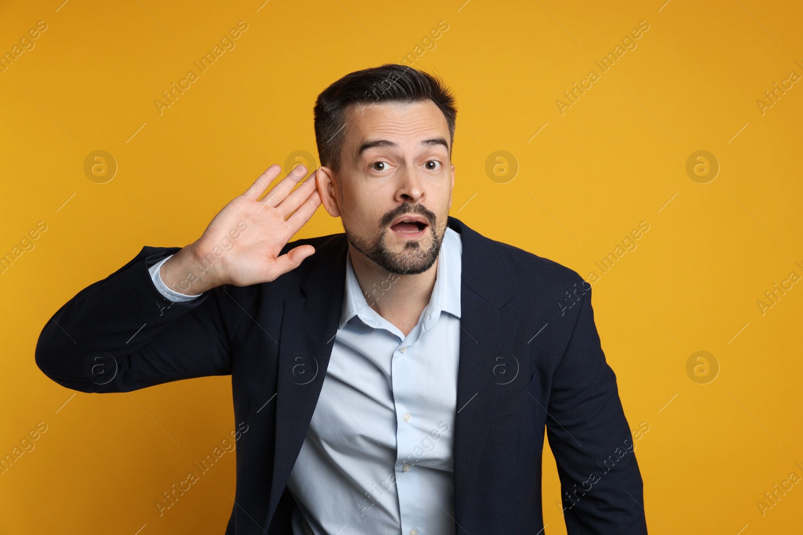 Photo of Man showing hand to ear gesture on orange background