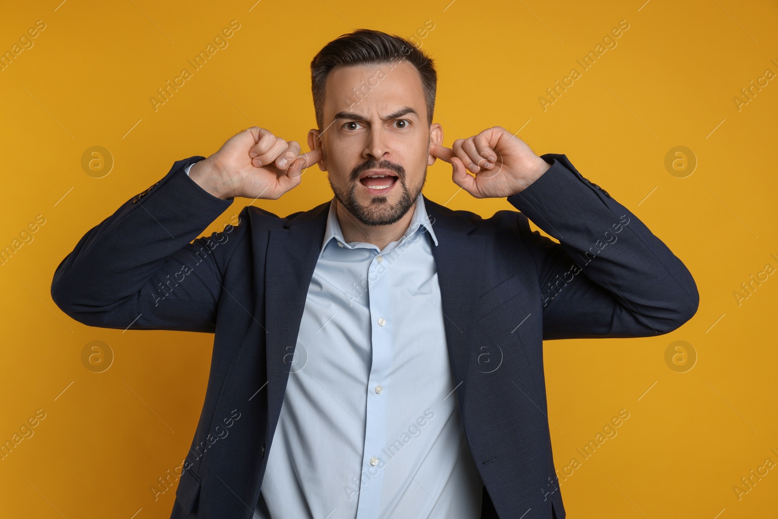 Photo of Man covering his ears with fingers on orange background