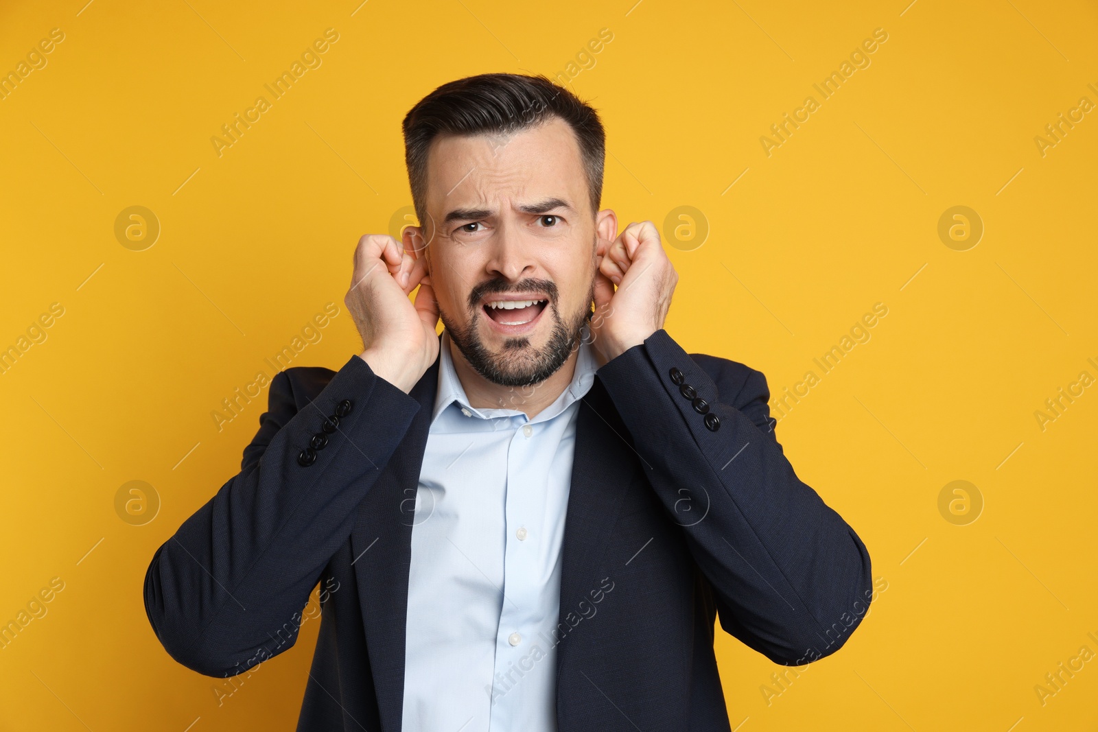 Photo of Man covering his ears with fingers on orange background