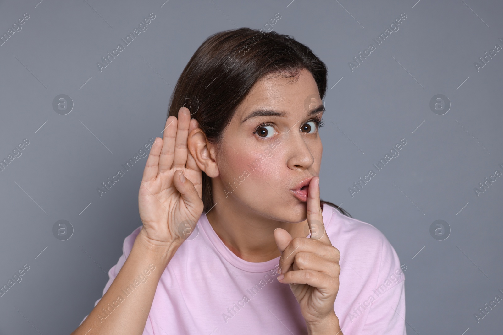 Photo of Woman showing hand to ear gesture on grey background