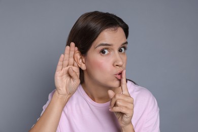 Photo of Woman showing hand to ear gesture on grey background