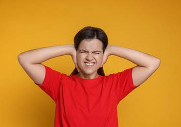 Woman covering her ears on orange background