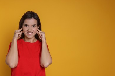 Woman covering her ears with fingers on orange background, space for text