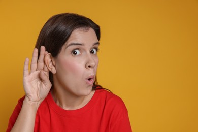 Photo of Woman showing hand to ear gesture on orange background, space for text