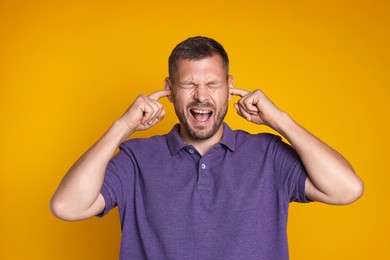 Photo of Man covering his ears with fingers on orange background