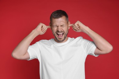 Photo of Man covering his ears with fingers on red background