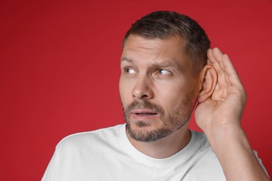 Photo of Man showing hand to ear gesture on red background