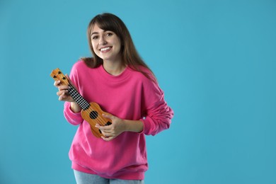 Happy woman playing ukulele on light blue background, space for text