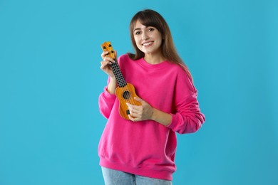 Happy woman playing ukulele on light blue background