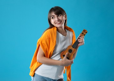 Photo of Happy woman playing ukulele on light blue background, space for text