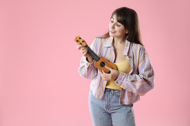 Happy woman playing ukulele on pink background, space for text