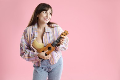 Happy woman playing ukulele on pink background, space for text